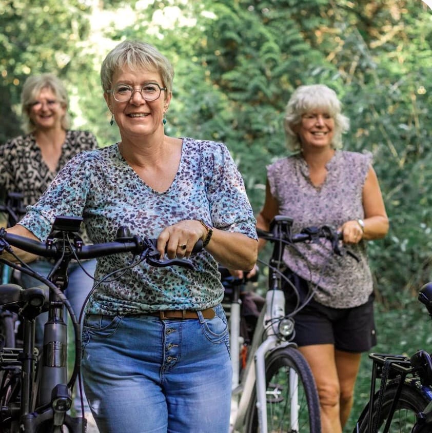 Drie vrouwen met hun fiets op een bospad